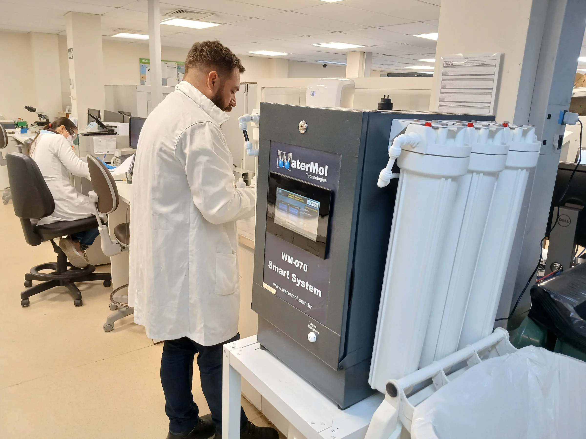 Técnico de jaleco operando equipamento de produção de água tipo 1 em laboratório clínico