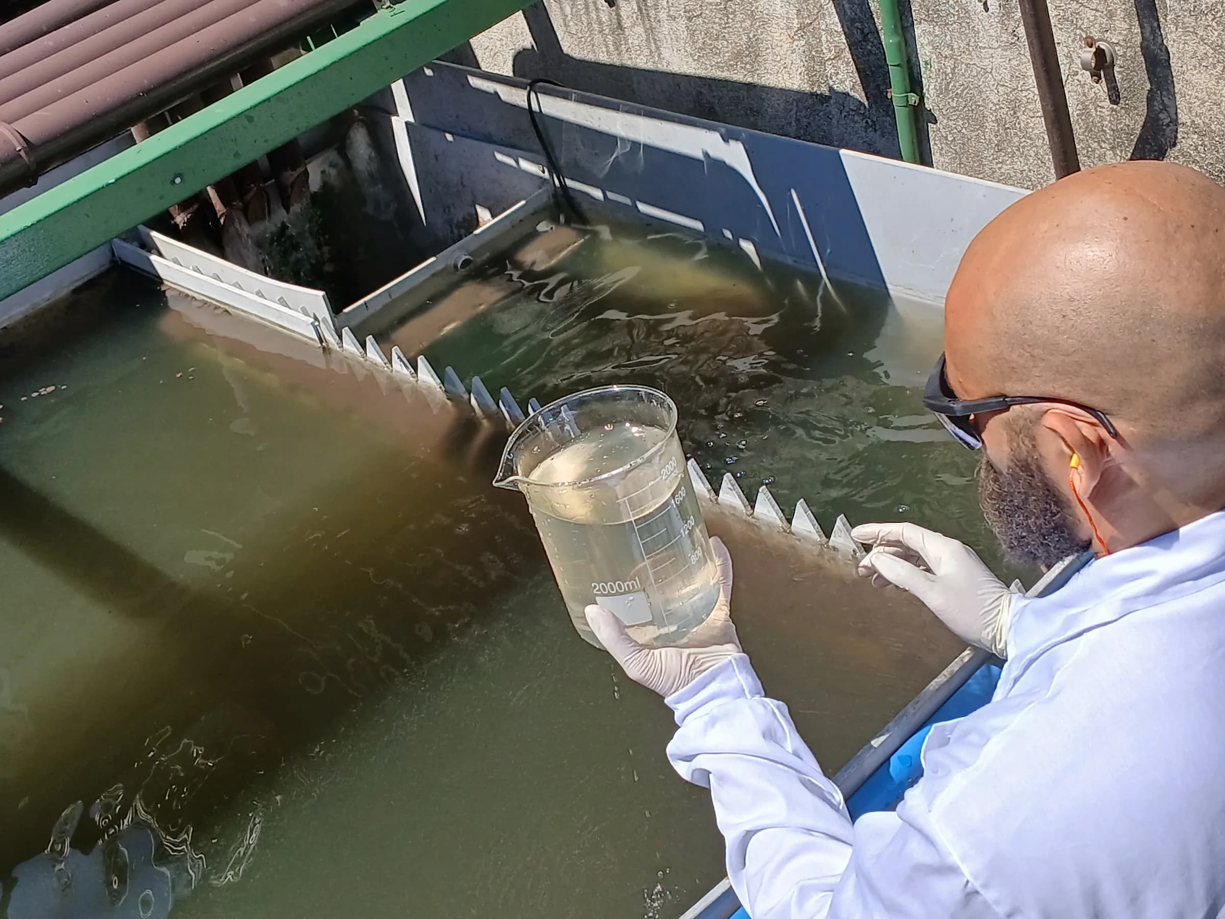 Técnico segurando béquer com amostra de água sobre tanque de aeração externo