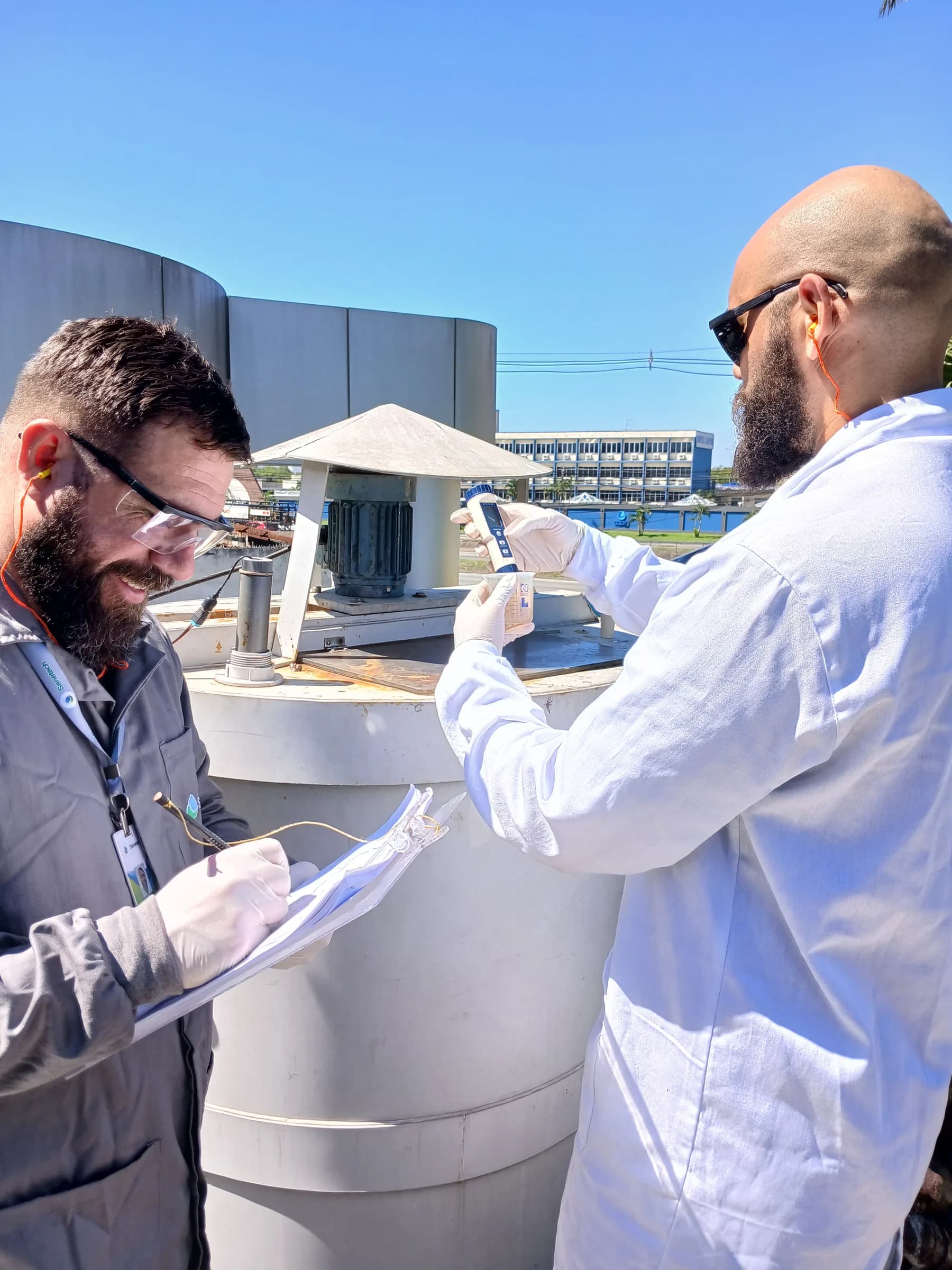 Dois técnicos coletando amostra em tanque externo com skyline urbano