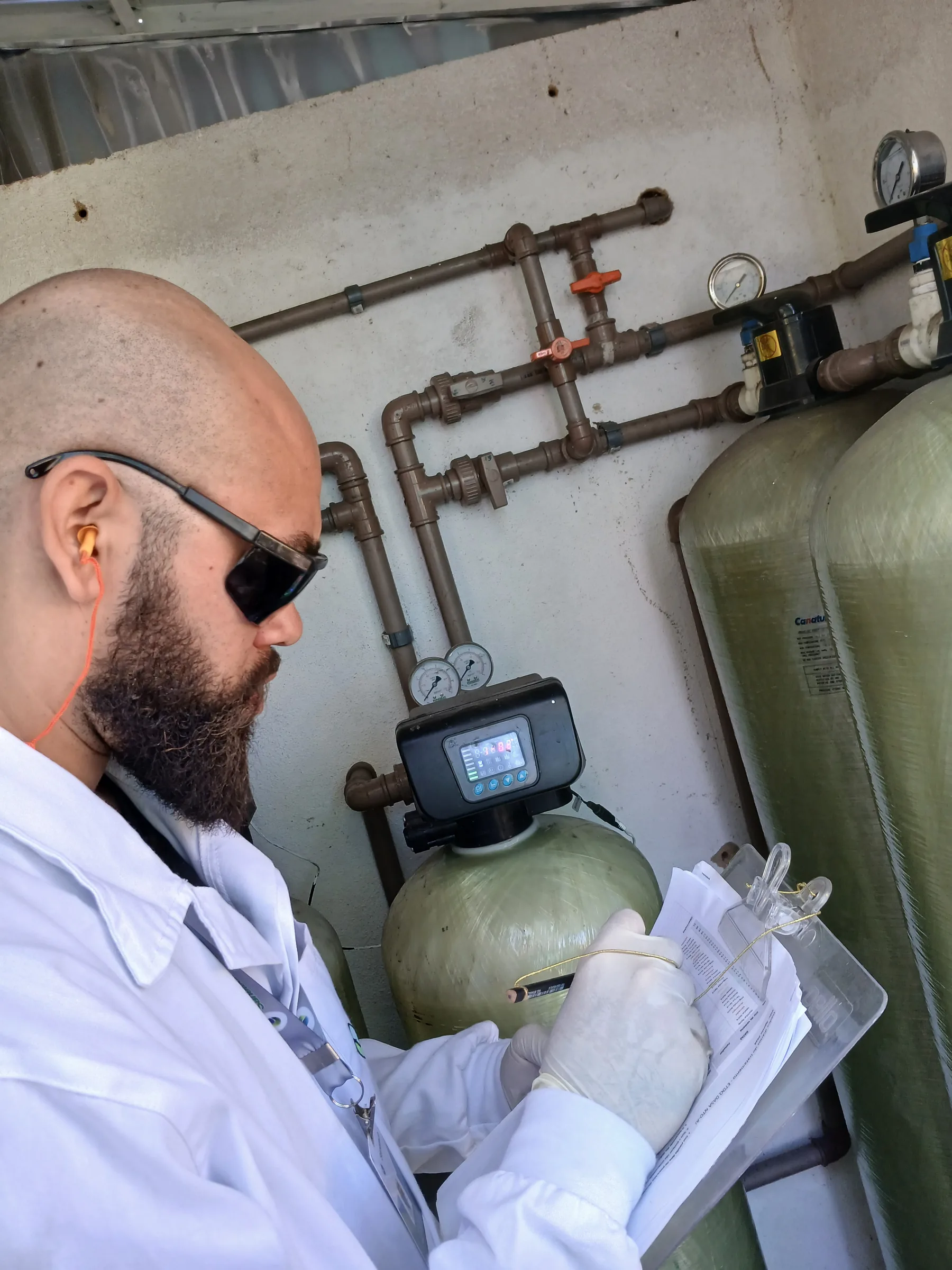 Técnico com clipboard analisando filtros pressurizados verdes em sala de tratamento