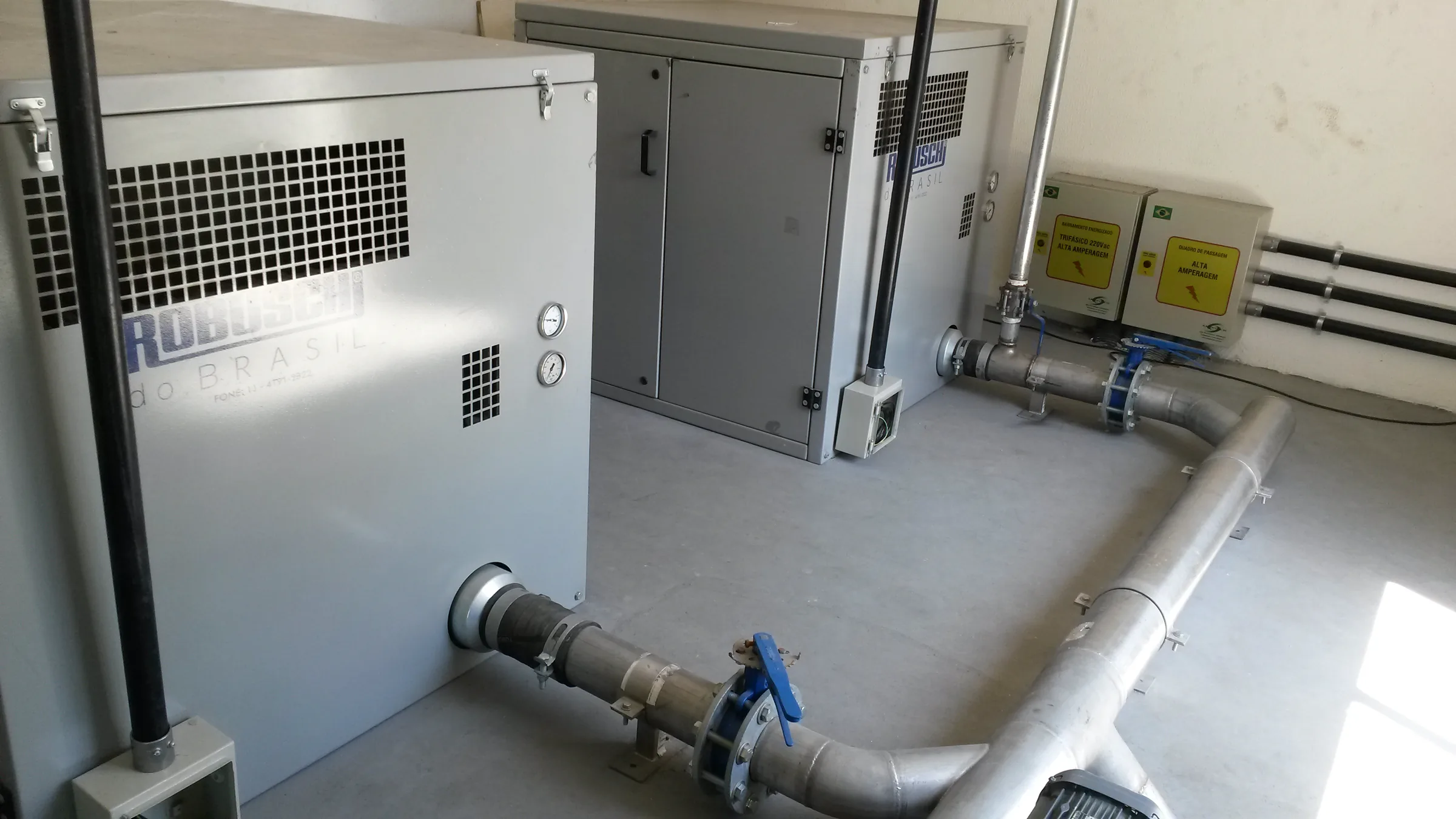 Sala de sopradores com compressores cinzas e tubulação metálica organizada